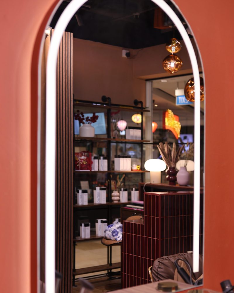 Arched LED-lit styling mirror reflecting the product shelves at One Degree Edit