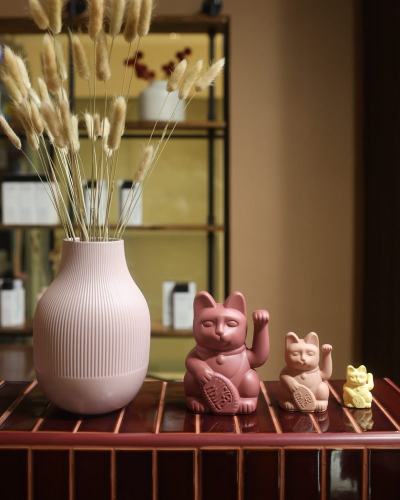 Pink lucky cats and a ribbed vase of dried pampas on the reception counter at One Degree Edit